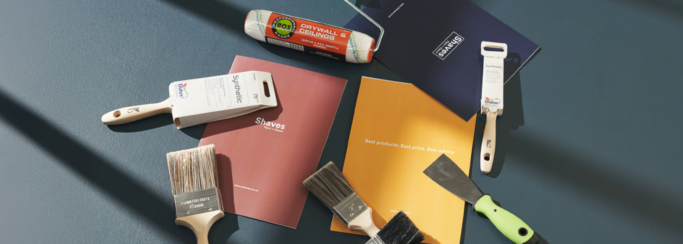 Assorted painting tools, colour brochures, and a scraper on a dark blue surface.