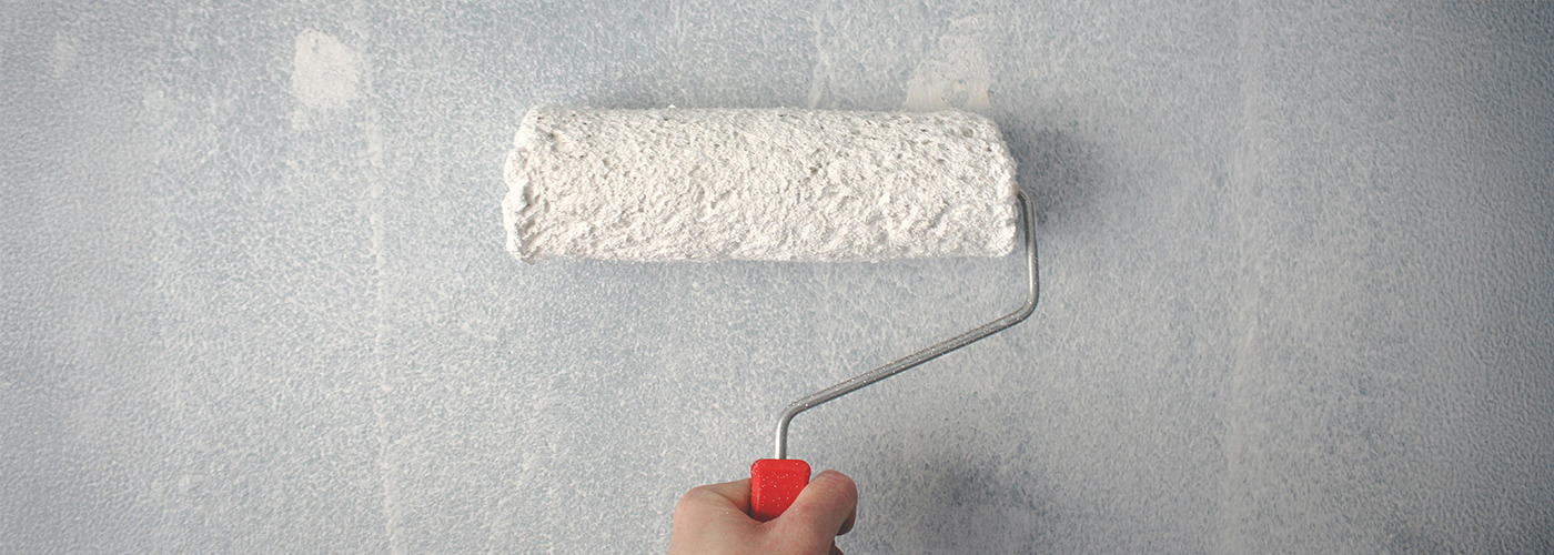 Hand using a paint roller to apply white paint on a blue-toned wall.