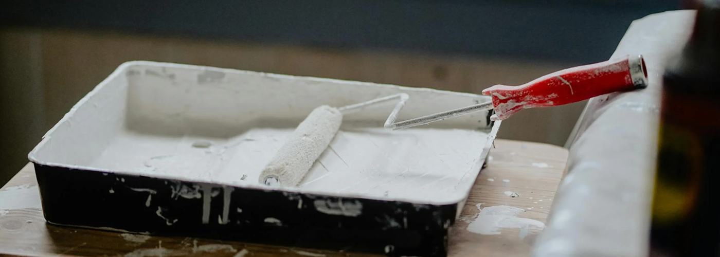 Paint tray with a roller covered in white paint resting on a wooden stool.