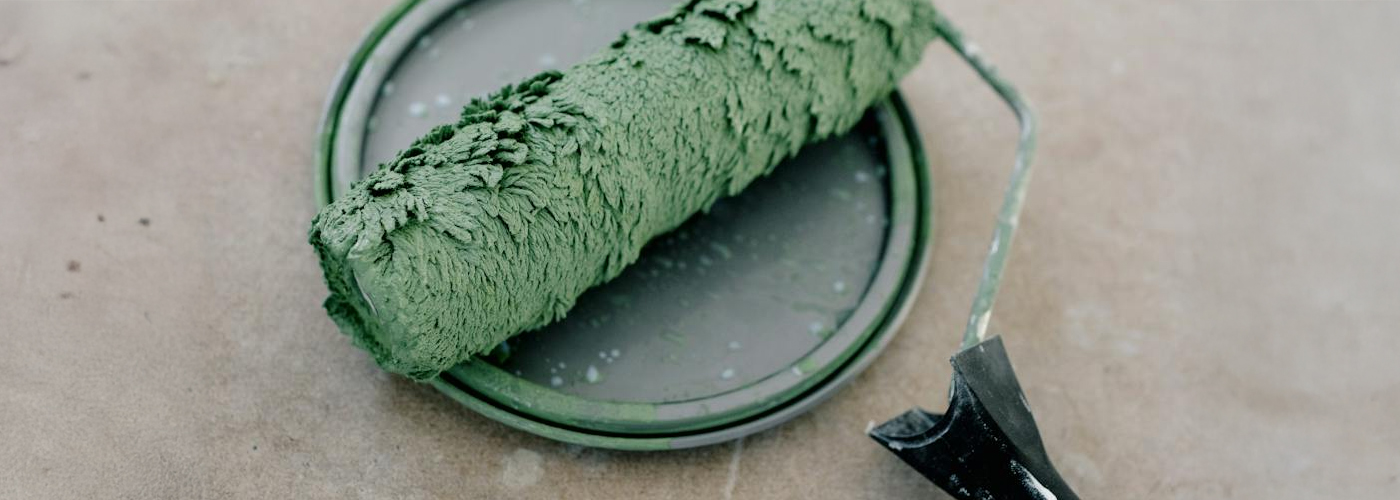 A green paint roller resting on the rim of a matching green paint tray.