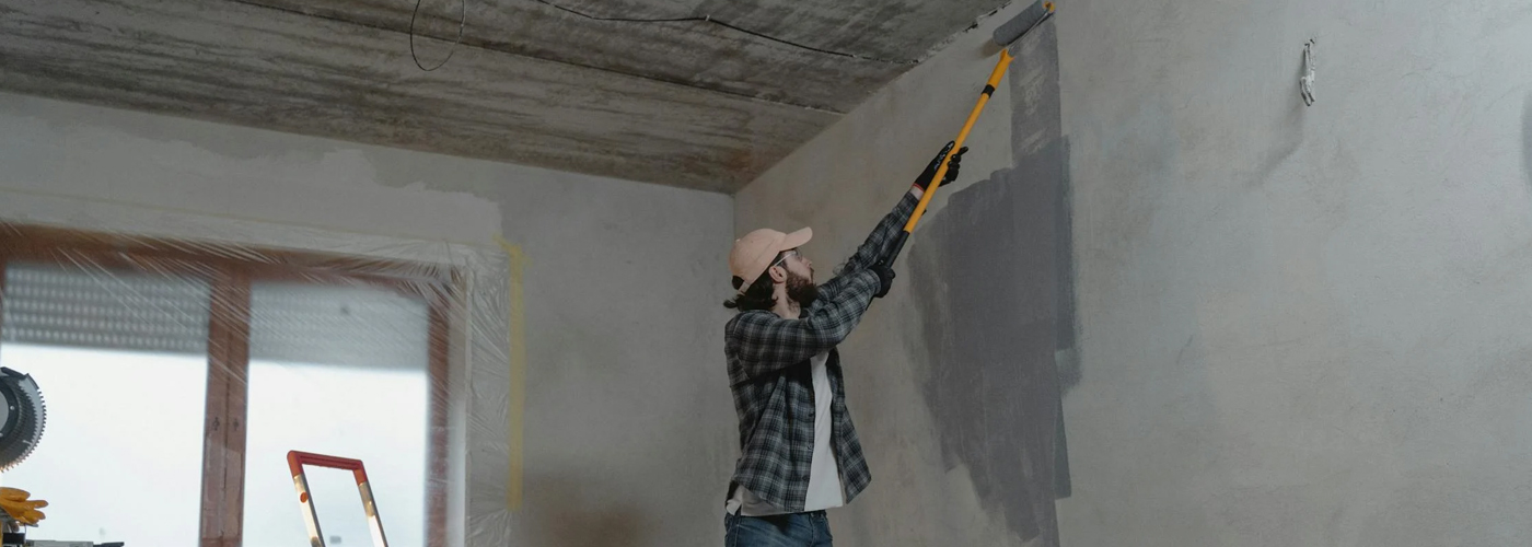 Person painting a wall grey using a roller on an extension pole.